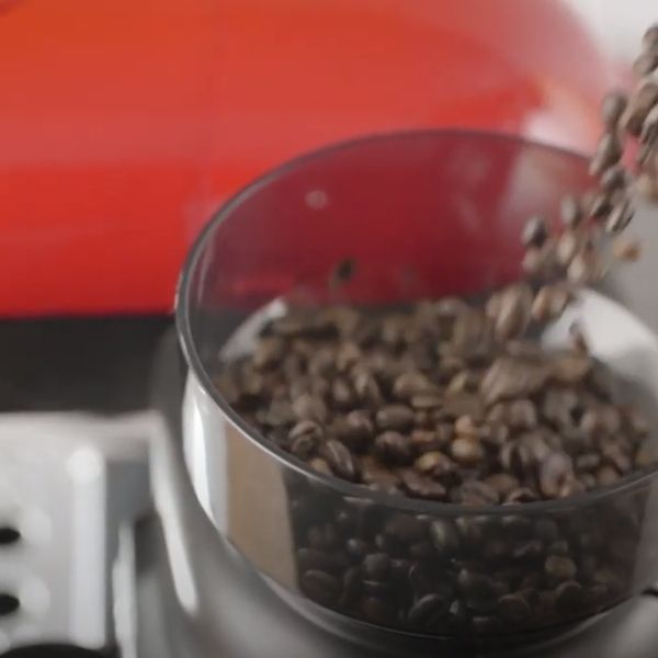 Кафени зърна се изсипват в мелничката на машина за еспресо от червена лъжичка.