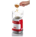 Ръка, изсипваща зърна пуканки в червено-бяла електрическа машина за пуканки.