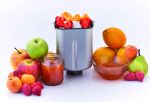 Разнообразие от пресни плодове, включително ябълки, портокали, круши, кайсии и ягоди, изложени около Хлебопекарна PANEXPRESS 1000 метален контейнер, пълен с нарязани плодове до буркани с плодове.