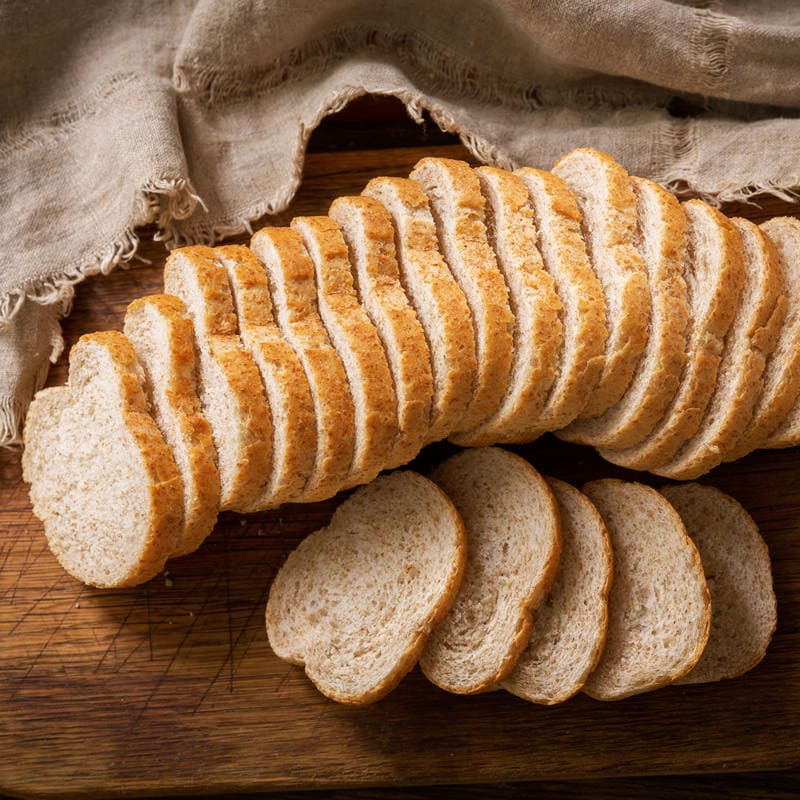 Нарязан хляб Хлебопекарна PANEXPRESS 1000 бял хляб върху дървена дъска за рязане с бежов плат на заден план.