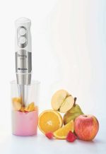 Пасатор PIMMY 500 3 в 1 потапящ се блендер, разположен до прозрачен съд с нарязани плодове, включително ябълка, круша, портокал и ягоди на бял фон.