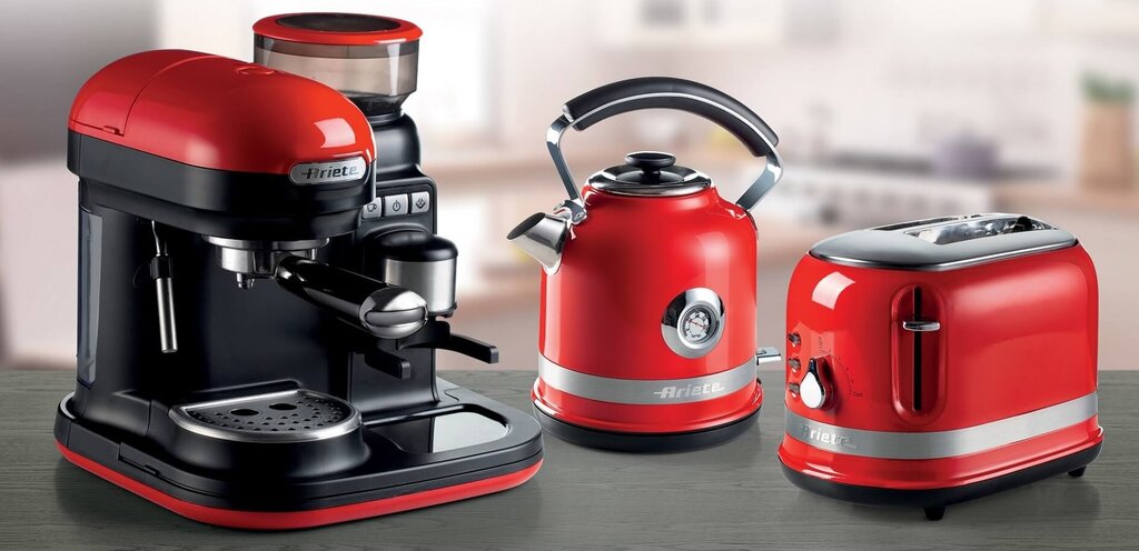 Червена машина за еспресо, чайник и тостер на кухненски плот, всички с метално покритие и надпис „ариете“.