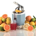 Електрическа сокоизстисквачка за цитрусови плодове, изцеждаща сок от портокал, заобиколен от различни цитрусови плодове на бял фон.