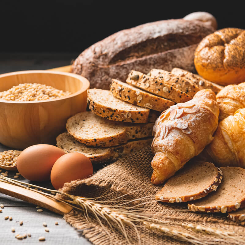 Асорти от хлебни изделия от Хлебопекарна PANEXPRESS 750, включително нарязан черен хляб, кроасани и пшенични зърна, с яйца върху покрита с чул повърхност.