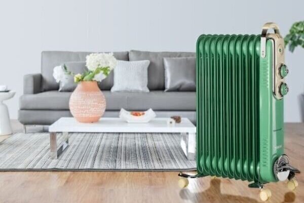 Зелен преносим радиатор в модерна всекидневна със сив диван, бяла масичка за кафе и декоративна розова ваза върху сив килим, закупен от магазин за електроуреди.