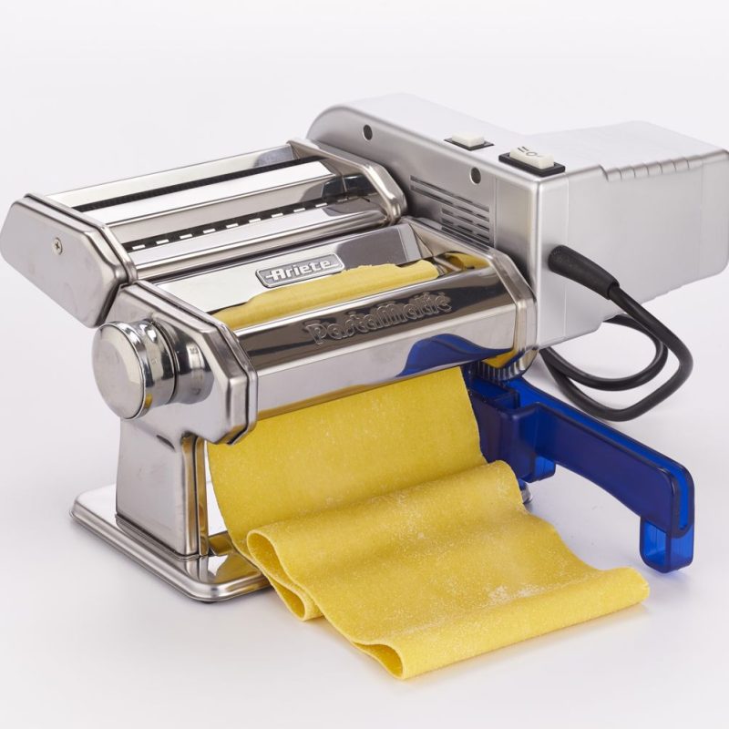 Електрическа машина за паста PASTAMATIC от неръждаема стомана с прясно жълто тесто за паста, което се разточва, поставено на бял фон.