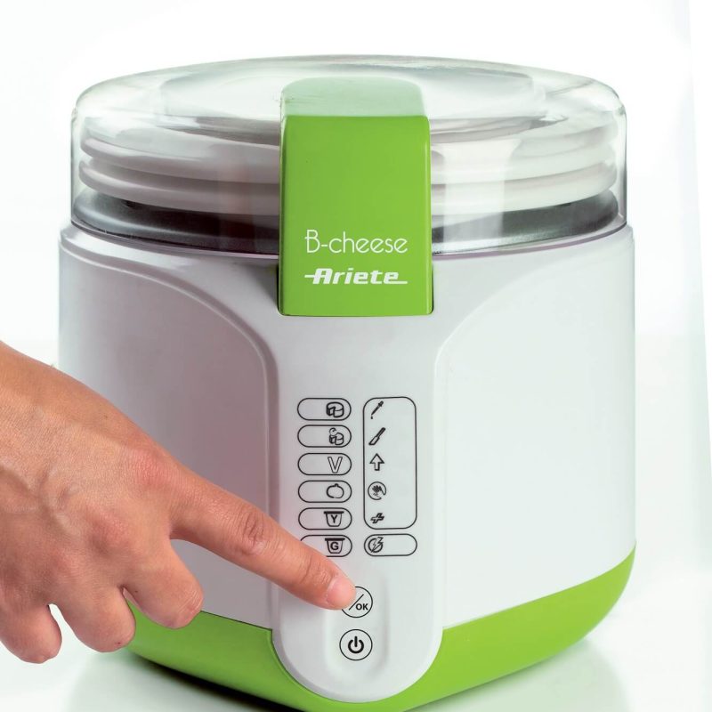 Пръстът на човек натиска бутон върху модерна, зелено-бяла машина за производство на сирене Ariete B-CHEESE, изложена на бял фон.