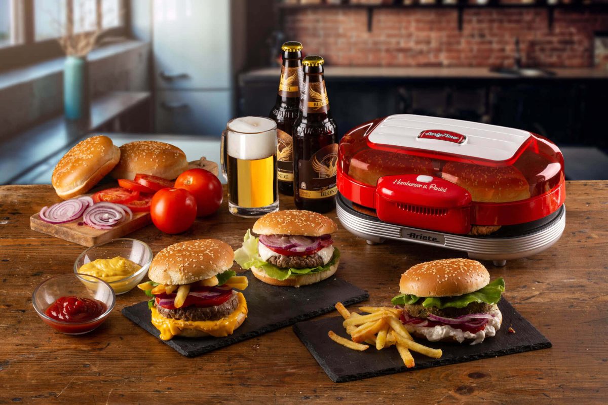 Описание: На стола се намира Уред за бургери и сандвичи Party Time с бургери, картофени фри и пиво.