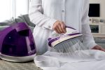 A woman is using a purple Център за гладене STEAM POWER to iron a white shirt.