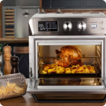 Фурната с горещ въздух и грил AIR FRYER OVEN 25 л пече цяло пиле и картофи; пържените картофи се въртят в кошница.