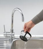 Ръчно изплакване на черен филтър Ariete под хромиран кухненски кран с течаща вода над мивка от неръждаема стомана.