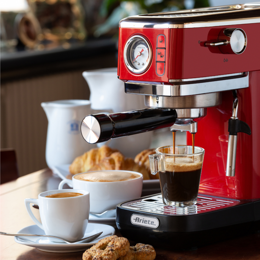 Кафемашина ESPRESSO SLIM MODERNA приготвя кафе в чаша, а на масата до нея са подредени сладкиши и чаши.