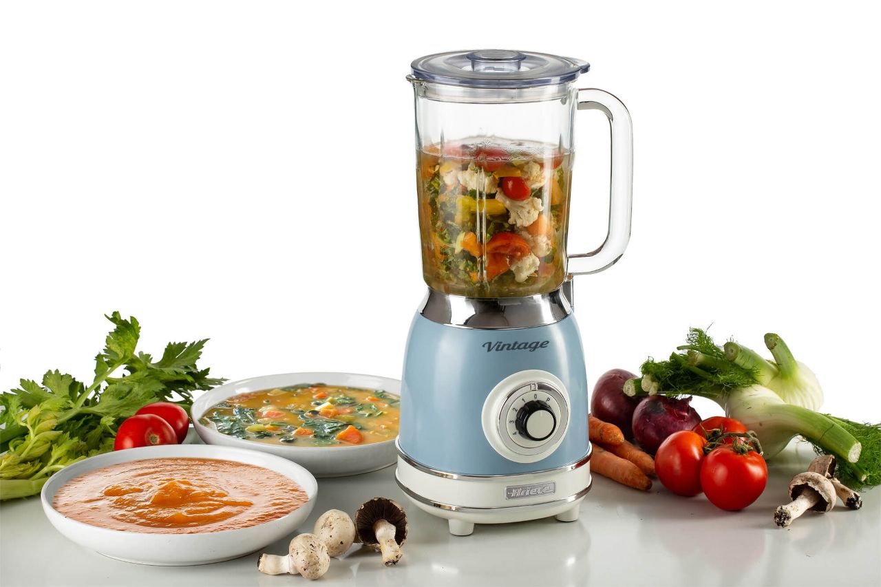 Блендер Ariete в ретро стил, пълен със зеленчуци, заобиколен от пресни продукти и купички с блендирани супи.