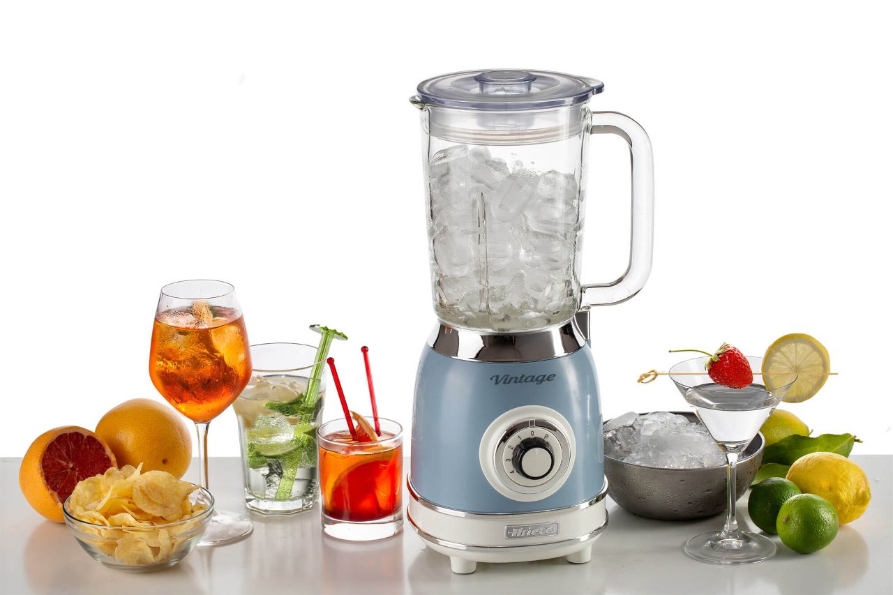 Блендер Ariete, пълен с лед, е заобиколен от три коктейла, плодове, леден чипс и купа с картофен чипс на масата.