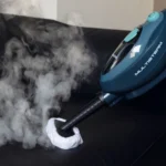 Парочистачката STEAM MOP 10 в 1 изпуска пара върху черна тапицирана повърхност с кърпа върху дюзата си.