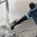 Парен пистолет VAPORÌ JET излъчва пара върху кухненски смесител над мивка от неръждаема стомана.