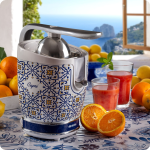 Цитрусова преса VINTAGE JUICER – „Капри“ със син мотив, портокали и чаши за сок на маса край морето.