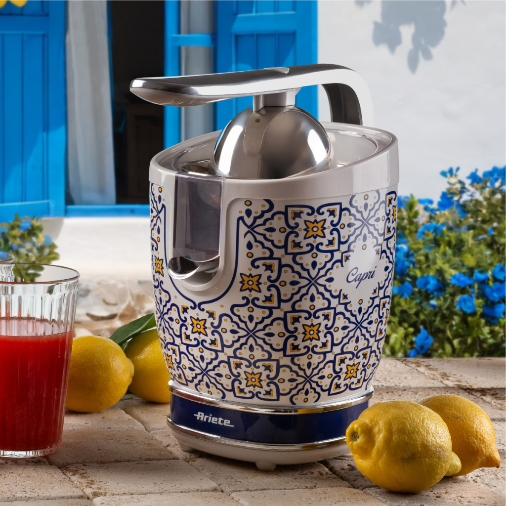 Цитрусова преса VINTAGE JUICER - Capri на масата с лимони и чаша червен сок, в стилен дизайн.