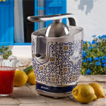 Цитрусова преса VINTAGE JUICER - Capri на масата с лимони и чаша червен сок, в стилен дизайн.