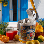 Цитрусовата преса VINTAGE JUICER – Positano с мотив от плочки е поставена до портокали и чаши за сок до синьо прозорче.