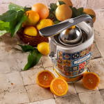 Цитрусовата преса VINTAGE JUICER – Positano стои на кухненския плот до нарязани портокали и кошница с цитрусови плодове.