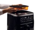Човек поставя капак на 7L AIR FRYER STEAM + GRILL с цифров контрол, показващ настройките.