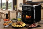 The Фритюрник с горещ въздух 4в1 AIR FRYER STEAM + GRILL 7л. на тезгяха с печено пиле, зеленчуци, пържола и олио.