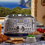 Тостер VINTAGE, за 4 филии – Capri стои на маса с препечен хляб, кроасани, плодове и прекрасна гледка към морето.