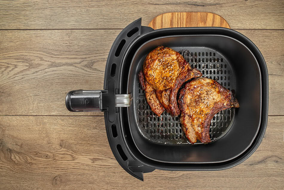 Еър фрайър кошница с варени свински пържоли подправени и подредени върху дървен плот.