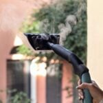 Една ръка използва парочистачката X-Vapor Comfort, 5 бара, за да изпуска пара на открито в близост до сграда и зеленина.