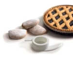 Един пай и три бисквити на прах се намират в близост до бял диспенсър за тиксо и Кухненски робот Vintage върху бяла повърхност.