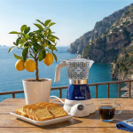 Лимоново дърво, препечен хляб и електрическа кафемашина „Moka Vintage Capri“ на маса с изглед към морето.