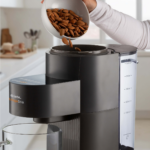 Някой изсипва цели бадеми в Уред за ядково мляко My Veggie Drink на кухненския плот.