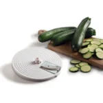 Три цели тиквички и нарязани тиквички върху дъска за рязане до острието на Кухненски робот Vintage slicer.