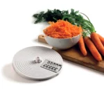 Кухненски робот Vintage с диск за настъргване е показан до настъргани моркови, цели моркови и магданоз върху дъска.