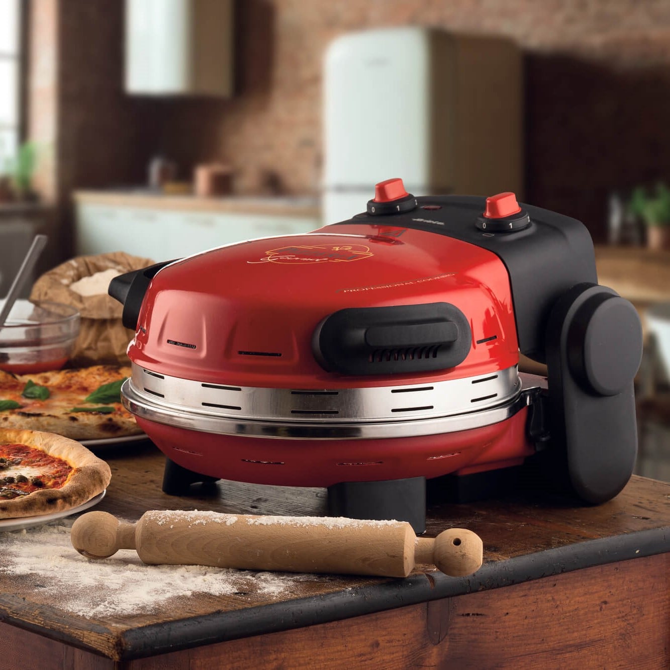 Червена Фурна за пица "Pizzeria Gourmet" стои на кухненски плот с точилка и съставки за пица.
