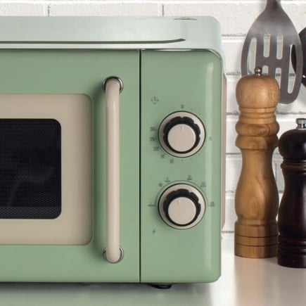 Зелена Микровълнова фурна Vintale 20L стои на кухненския плот в близост до сол, мелнички за пипер и прибори.