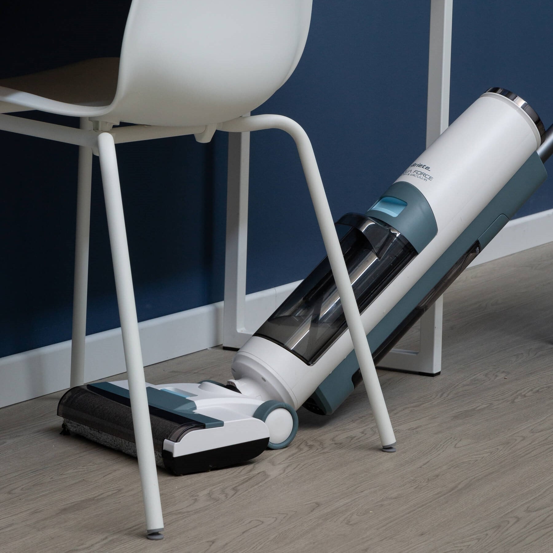 Вертикална прахосмукачка Aqua Force Wash & Vacuum почиства под бял стол върху светъл дървен под.