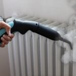 Човек почиства бял радиатор с парочистачка X-Vapor Comfort, 5 бара, като отделя видима пара.