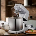 Сребрист Планетарен миксер Gourmet Supreme 10L стои до тестото и пресния хляб на плота.