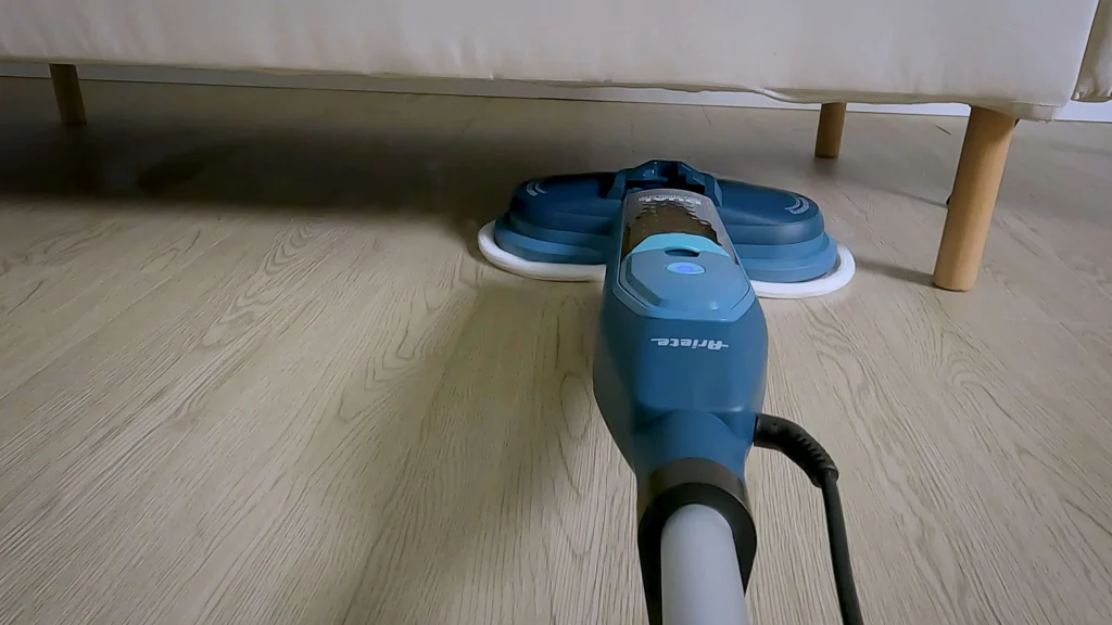 Парочистачка Dual Steam Scrub с въртящ се моп почиства светъл дървен под под диван.