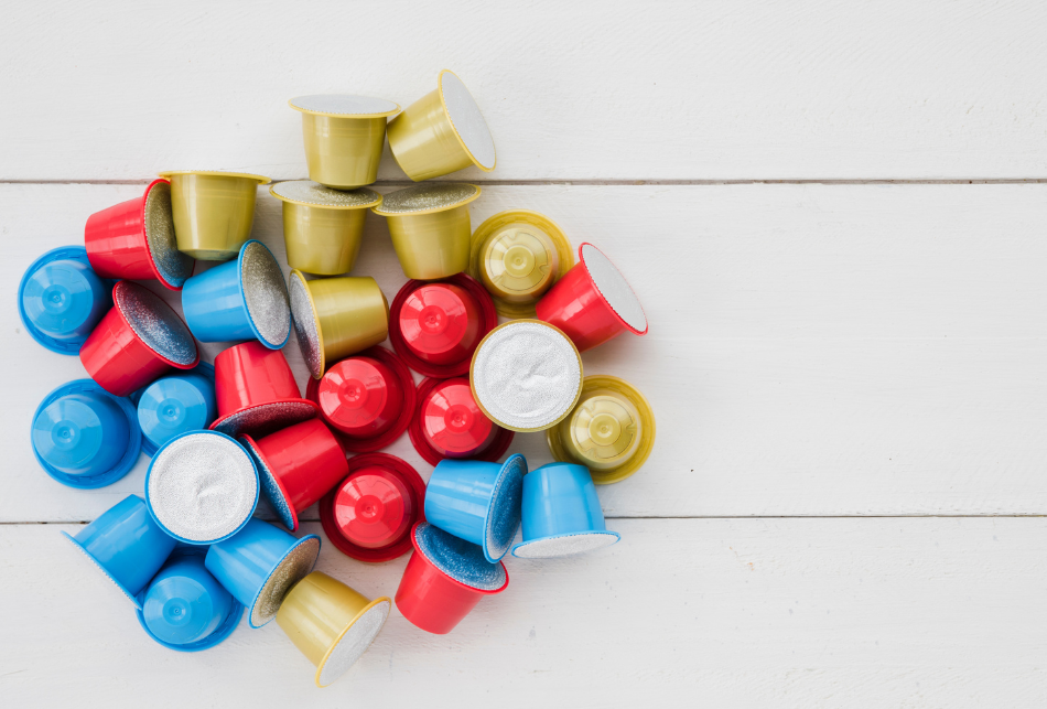 Купчина разноцветни капсули за кафе върху бяла дървена повърхност-научете как да изхвърляме кафе капсули правилно.