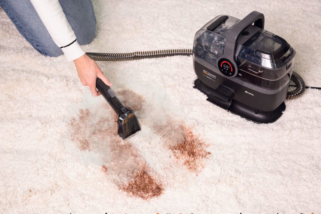 Някой използва уреда за почистване на петна „Spot Cleaner Steam Pro 5in1“, за да премахне кафяво петно от бял килим.