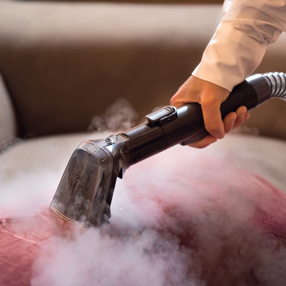 Някой почиства червена тъкан с уреда за отстраняване на петна Spot Cleaner Steam Pro 5in1, като по време на почистването се вижда пара.
