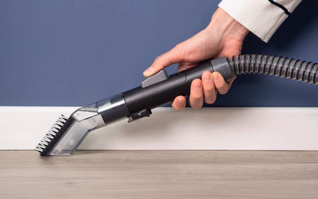 Ръка използва уреда за почистване на петна Spot Cleaner Steam Pro 5in1, за да почисти праха по дървената перваза.