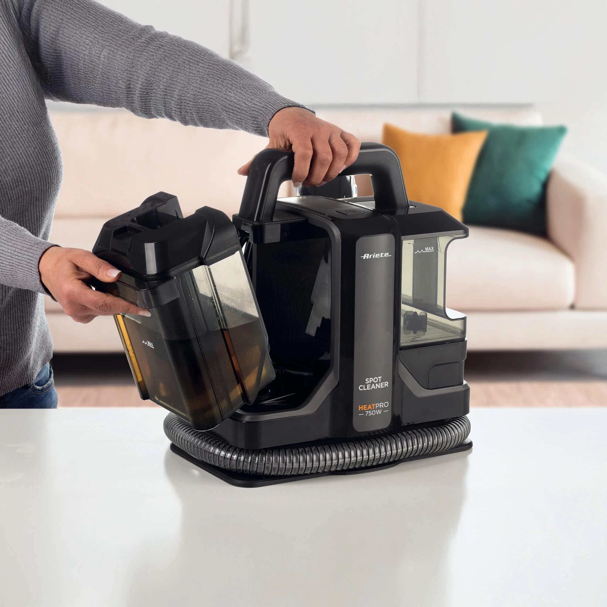 Човек изважда резервоара за мръсна вода от уреда за почистване на петна „Spot Cleaner Heat Pro“, поставен върху бял плот.