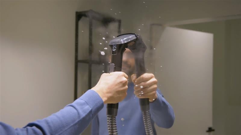 Човек, който почиства огледало с уреда за отстраняване на петна Spot Cleaner Steam Pro 5in1, като от уреда се издига пара.