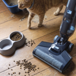 Прахосмукачката за мокро и сухо почистване AquaForce Easy Wash & Vacuum събира разсипаната котешка храна и пълнеж от дървения под. Наблизо една котка любопитно минава покрай автоматична машина за сладолед, докато на пода до разхвърляното място стои купа с храна.