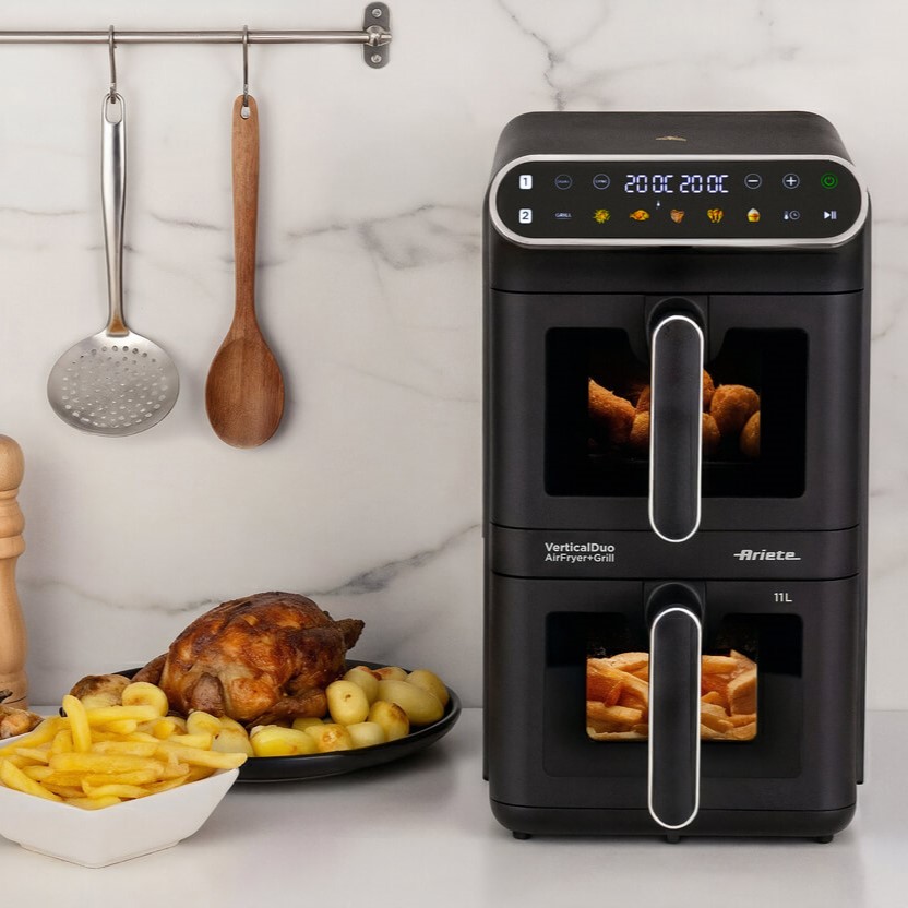 Фритюрник с горещ въздух с две кошници „Air Fryer Vertical Duo“, с обем 11 л и готова храна, стои на кухненския плот до чиния с печено пиле, картофи и пържени картофи; наблизо, робот-прахосмукачка с Wi-Fi е готова да поддържа пода чист, докато приборите висят на стената отгоре.